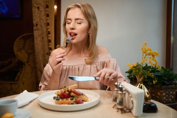 Lady enjoying taste of fresh berries and waffles at cafe